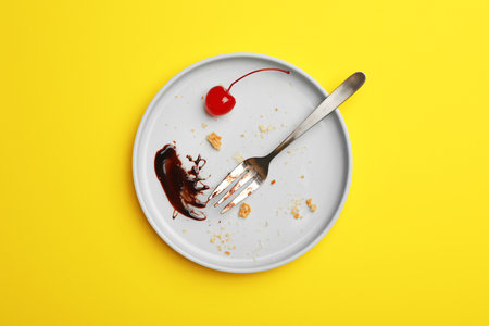 Dirty plate with food leftovers, fork and canned cherry on yellow background, top viewの写真素材