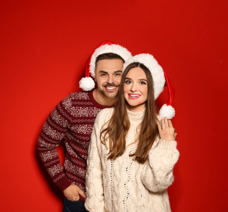 Couple wearing Christmas sweaters and Santa hats on red backgroundの写真素材