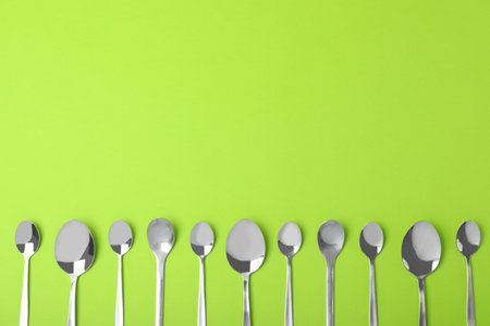 New metal spoons on green background, flat lay with space for textの写真素材