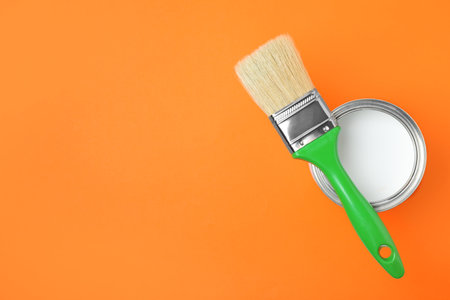Open can with white paint and brush on orange background, top view. Space for textの写真素材