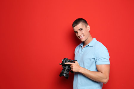 Young photographer with professional camera on red background. Space for text