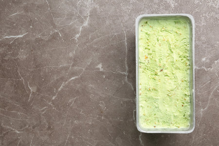 Container of sweet pistachio ice cream on brown marble table, top view. Space for textの写真素材