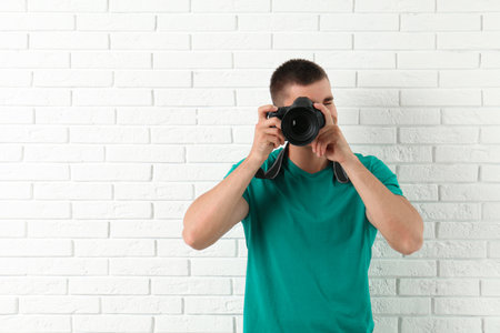 Young professional photographer taking picture near brick wall. Space for textの写真素材