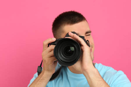 Young professional photographer taking picture on pink backgroundの写真素材