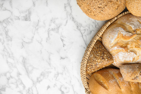 Loaves of different breads on white marble background, flat lay. Space for textの写真素材