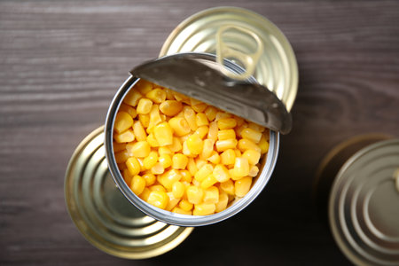 Open tin can of sweet corn and conserves on wooden table, top viewの写真素材