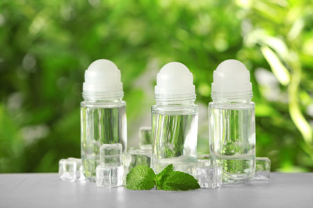 Deodorant containers, ice cubes and mint on white wooden table against blurred background