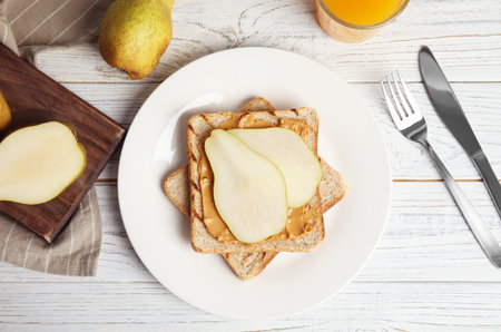 Slice of bread with peanut butter and pear on white wooden table, flat layの写真素材