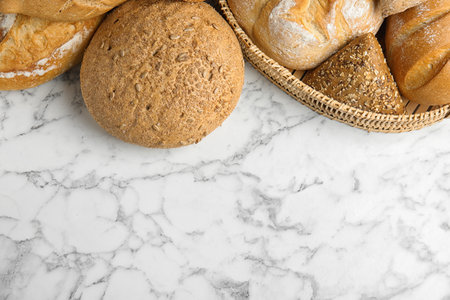 Loaves of different breads on white marble background, flat lay. Space for textの写真素材