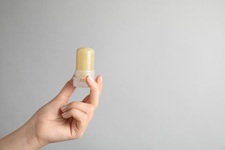 Young woman holding natural crystal alum deodorant on light gray background, closeup. Space for textの写真素材