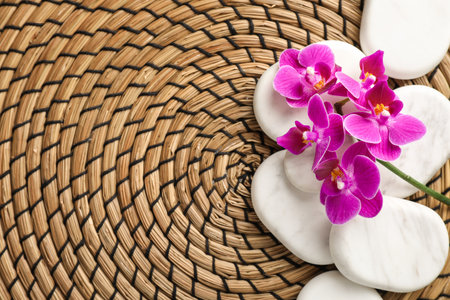 Spa stones and orchid flowers on wicker mat, top view. Space for textの写真素材