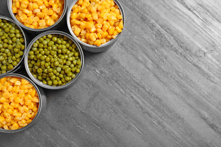 Open tin cans of canned vegetables on gray table, flat lay with space for text