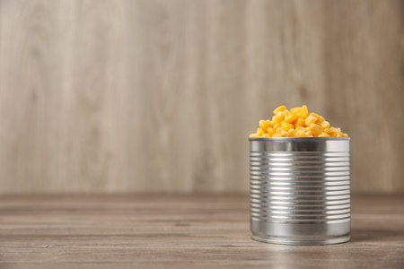 Open tin can of sweet corn on wooden table, space for textの写真素材