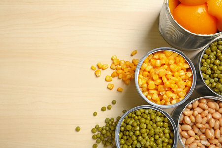 Open tin cans of canned vegetables on wooden background, flat lay with space for textの写真素材