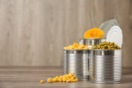 Open tin cans with canned vegetables and fruits on wooden table. Space for textの写真素材
