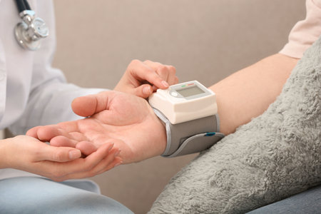 Nurse measuring blood pressure of elderly man against gray background, closeup. Assisting senior...