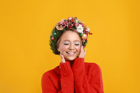 Beautiful young woman wearing Christmas wreath on yellow backgroundの写真素材