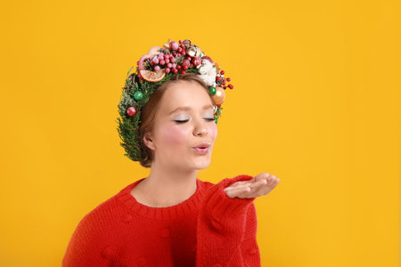 Beautiful young woman wearing Christmas wreath on yellow backgroundの写真素材