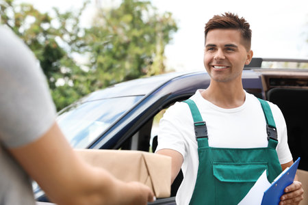 Young delivery courier with clipboard giving parcel to customer outdoors
