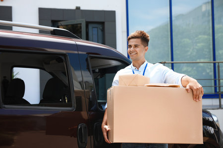 Young courier with parcels near delivery car outdoorsの写真素材