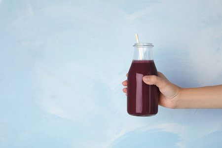 Woman with bottle of fresh acai drink and straw on light blue background, closeup. Space for textの写真素材