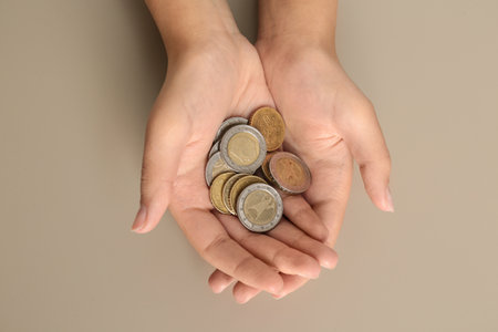 Young woman with handful of coins on beige background, top viewの写真素材