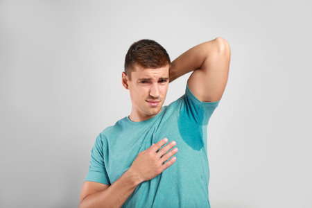 Young man with sweat stain on his clothes against light background. Using deodorantの写真素材
