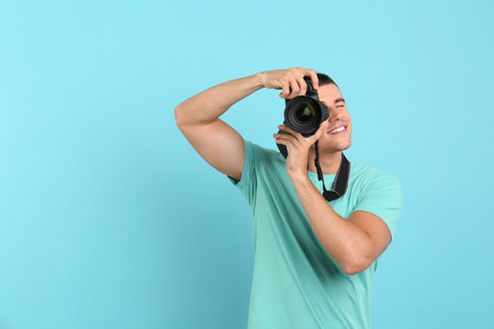 Young professional photographer taking picture on light blue background. Space for textの写真素材