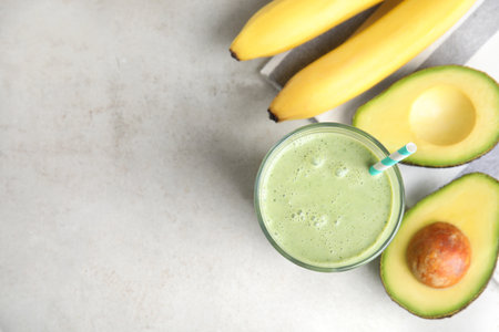 Glass of tasty smoothie, avocado and bananas on light gray table, flat lay. Space for text