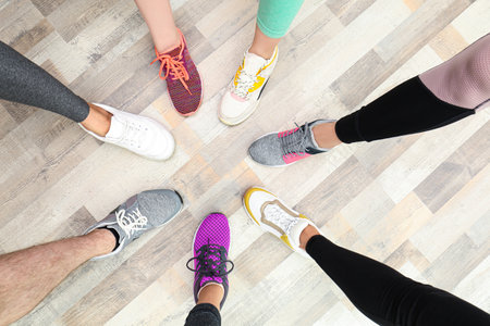 Closeup of athletes wearing sports shoes and standing in circle on wooden floor, top view