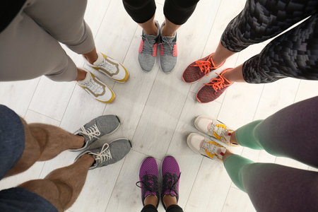 Closeup of athletes wearing sports shoes and standing in circle on wooden floor, top view. Space for...