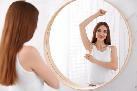 Beautiful young woman applying deodorant in bathroomの写真素材
