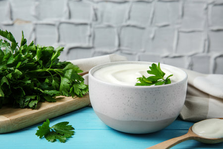 Bowl of fresh sour cream with parsley and spoon on light blue wooden tableの写真素材