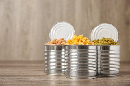 Open tin cans with canned vegetables on wooden table. Space for text