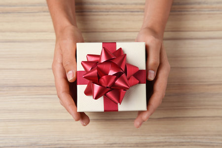 Woman holding beautiful gift box over wooden table, top viewの写真素材