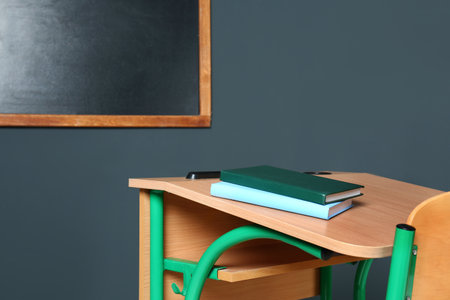 Wooden school desk with stationery near blackboard on gray wallの写真素材