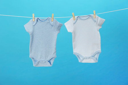 Baby bodysuits hanging on clothes line against blue background. laundry day