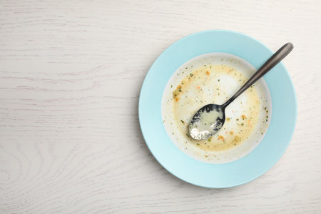 Dirty plate with food leftovers and spoon on white wooden background, top view. Space for textの写真素材