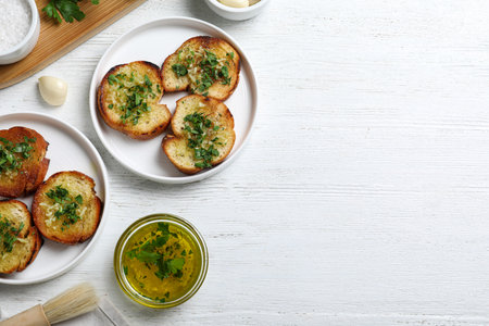 Slices of toasted bread with garlic and herb on white wooden table, flat lay. Space for textの写真素材
