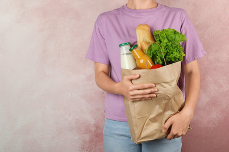 Woman holding shopping paper bag with different groceries against pink background. Space for textの写真素材