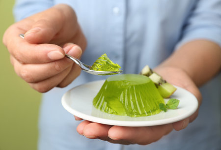 Young woman eating tasty kiwi jelly on green background, closeup