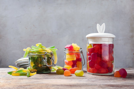 Glass jars and tasty jelly candies on wooden table against light background, space for textの写真素材