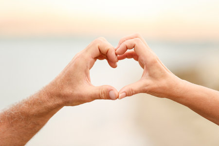 Happy couple making heart with their hands against blurred landscapeの写真素材