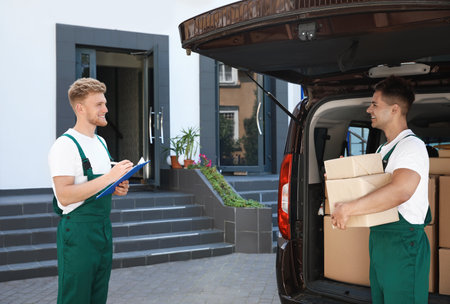 Young couriers with parcels near delivery car outdoors