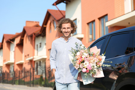 Young handsome man with beautiful flower bouquet near car on streetの写真素材
