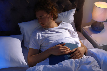 Handsome young man sleeping with book on pillow at night. Bedtimeの写真素材
