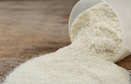 Overturned measuring scoop with protein powder on wooden table, closeupの写真素材