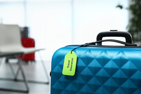 Blue suitcase with TRAVEL INSURANCE label indoors, closeup. Space for textの写真素材