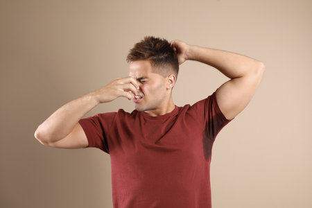 Young man with sweat stain on his clothes against beige background. Using deodorantの写真素材