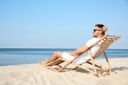 Young man relaxing in deck chair on sandy beachの写真素材